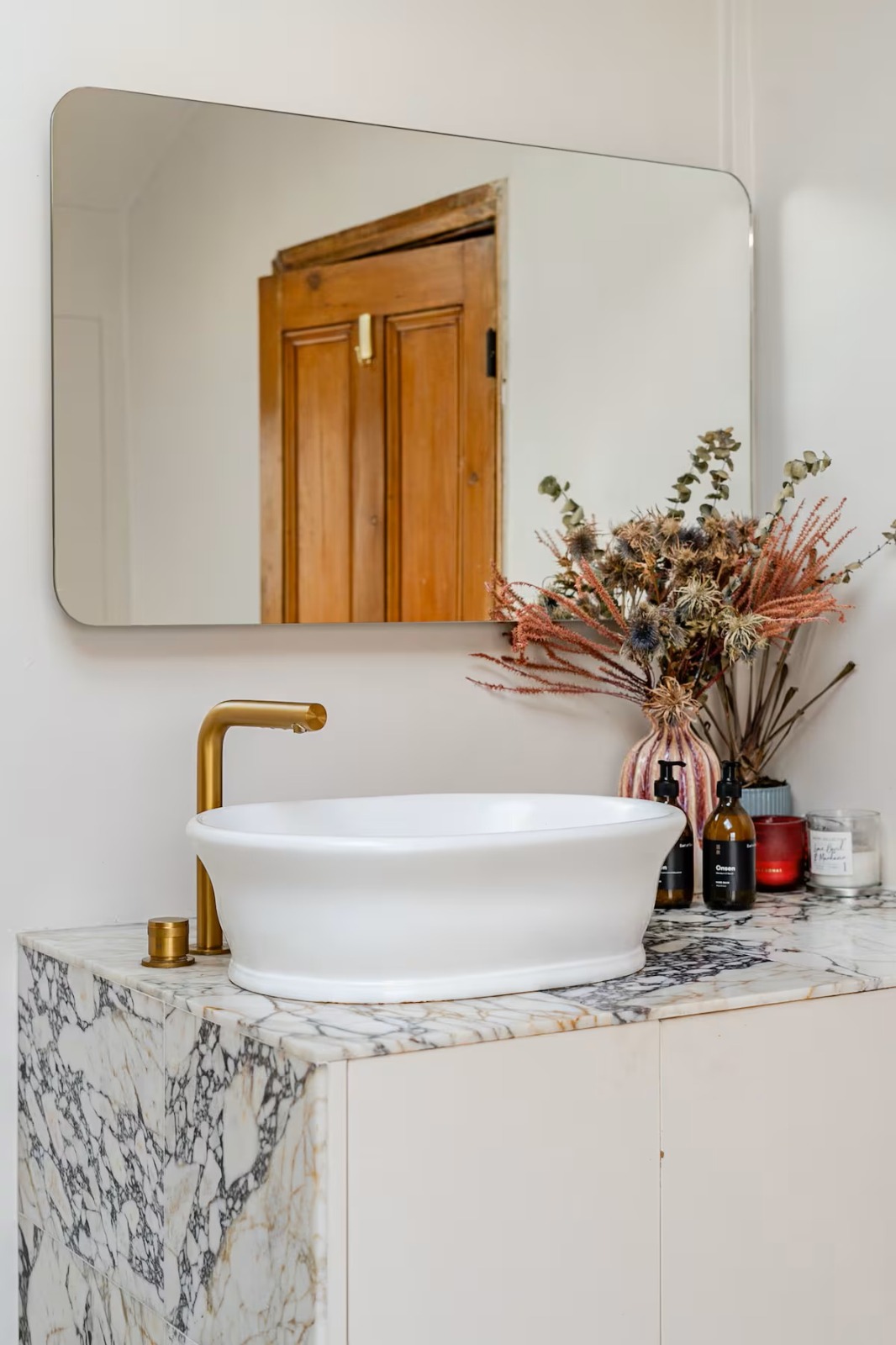 A marble washstand with brass tap, dried flowers and a rounded mirror